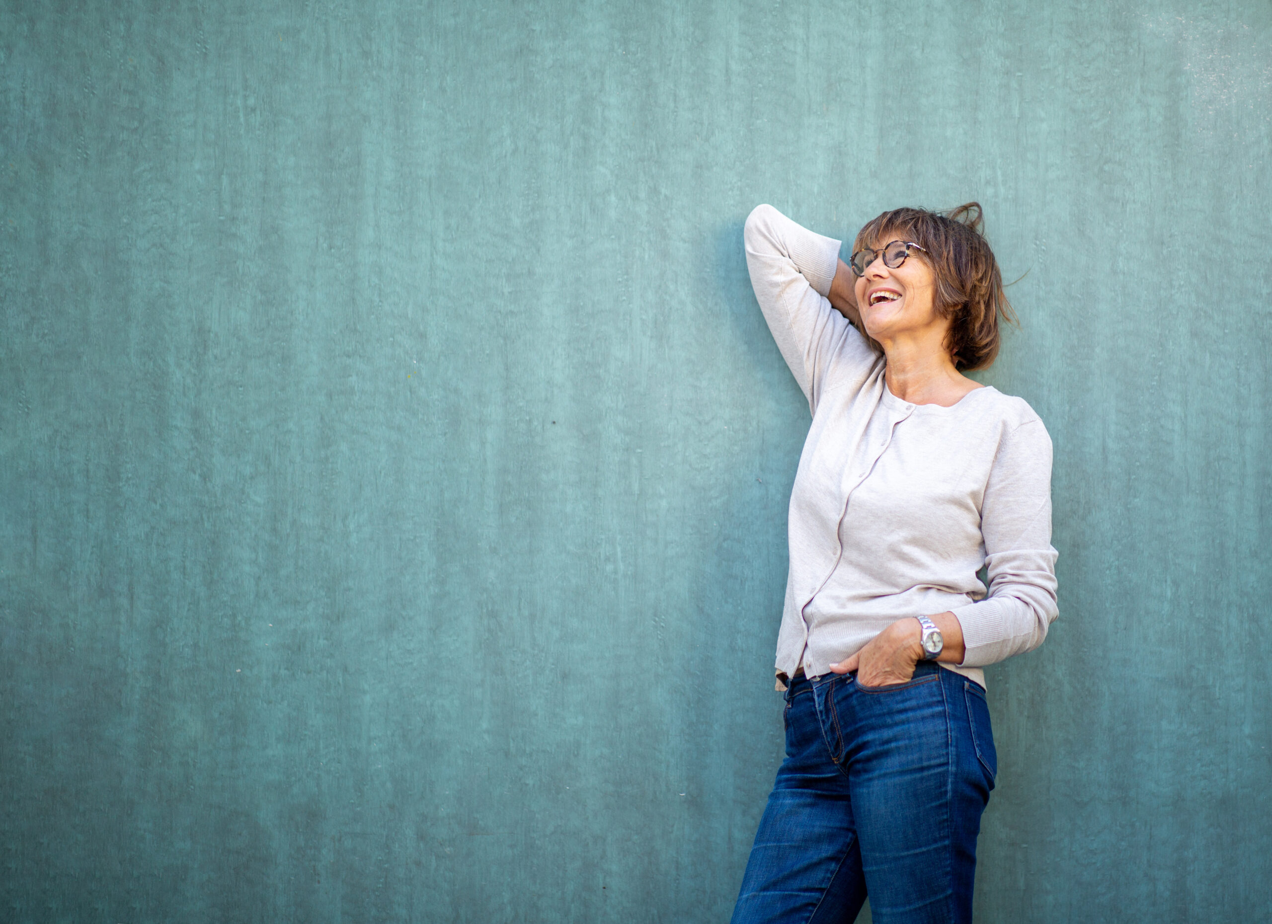happy older woman leaning against green wall