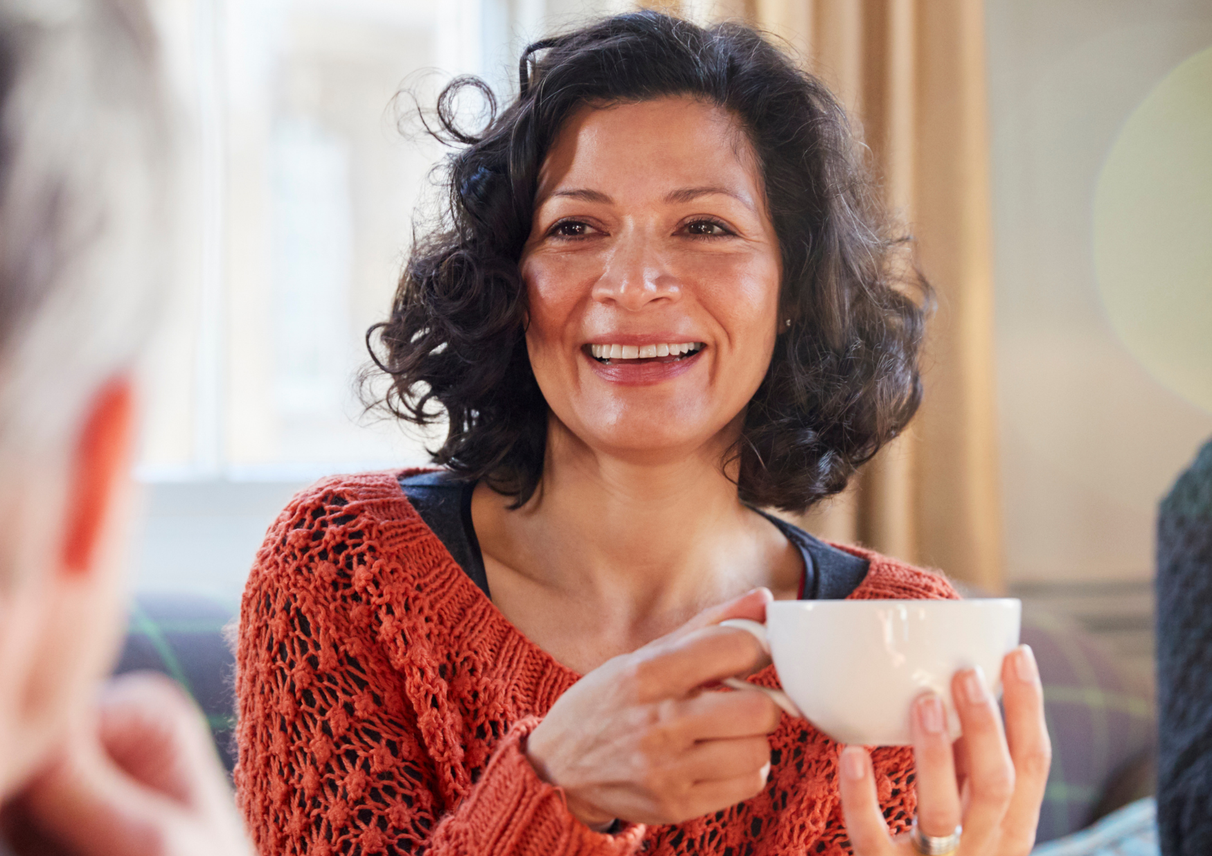 Latina middle-aged woman holding a white coffee cup and smiling