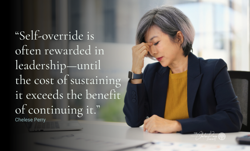 Woman pinching her eyebrows in stress while sitting at a white desk.